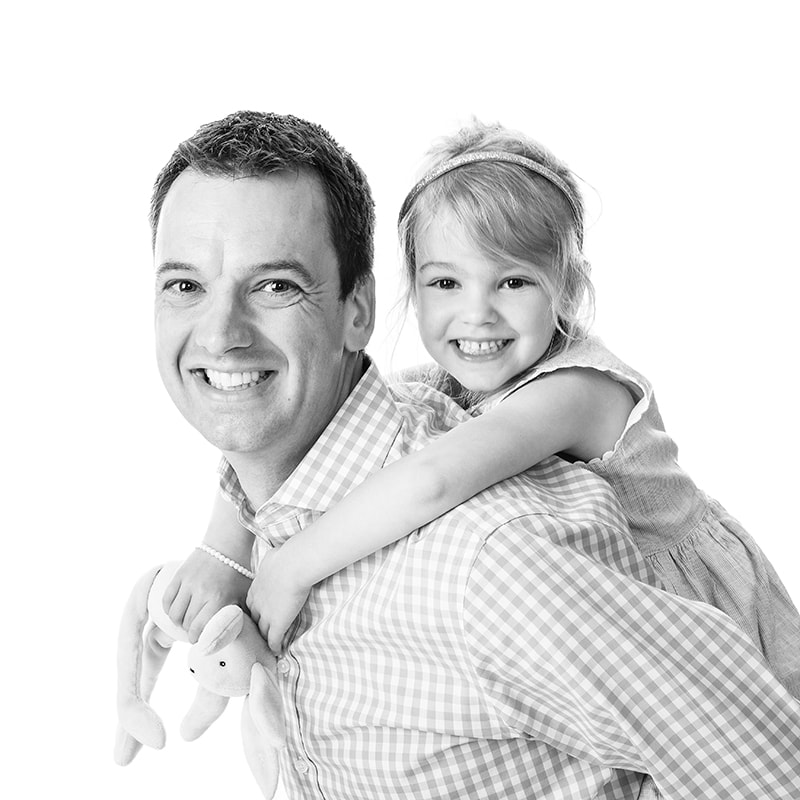 Black and white portrait of daughter on the back of her dad both smiling at camera.