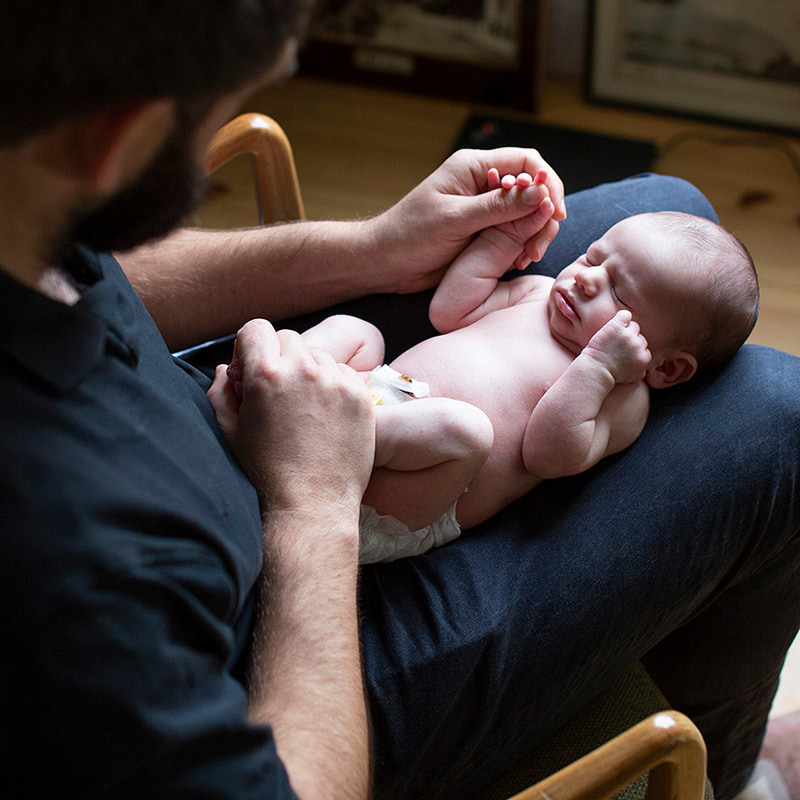 Newborn photo of baby on dads lap.