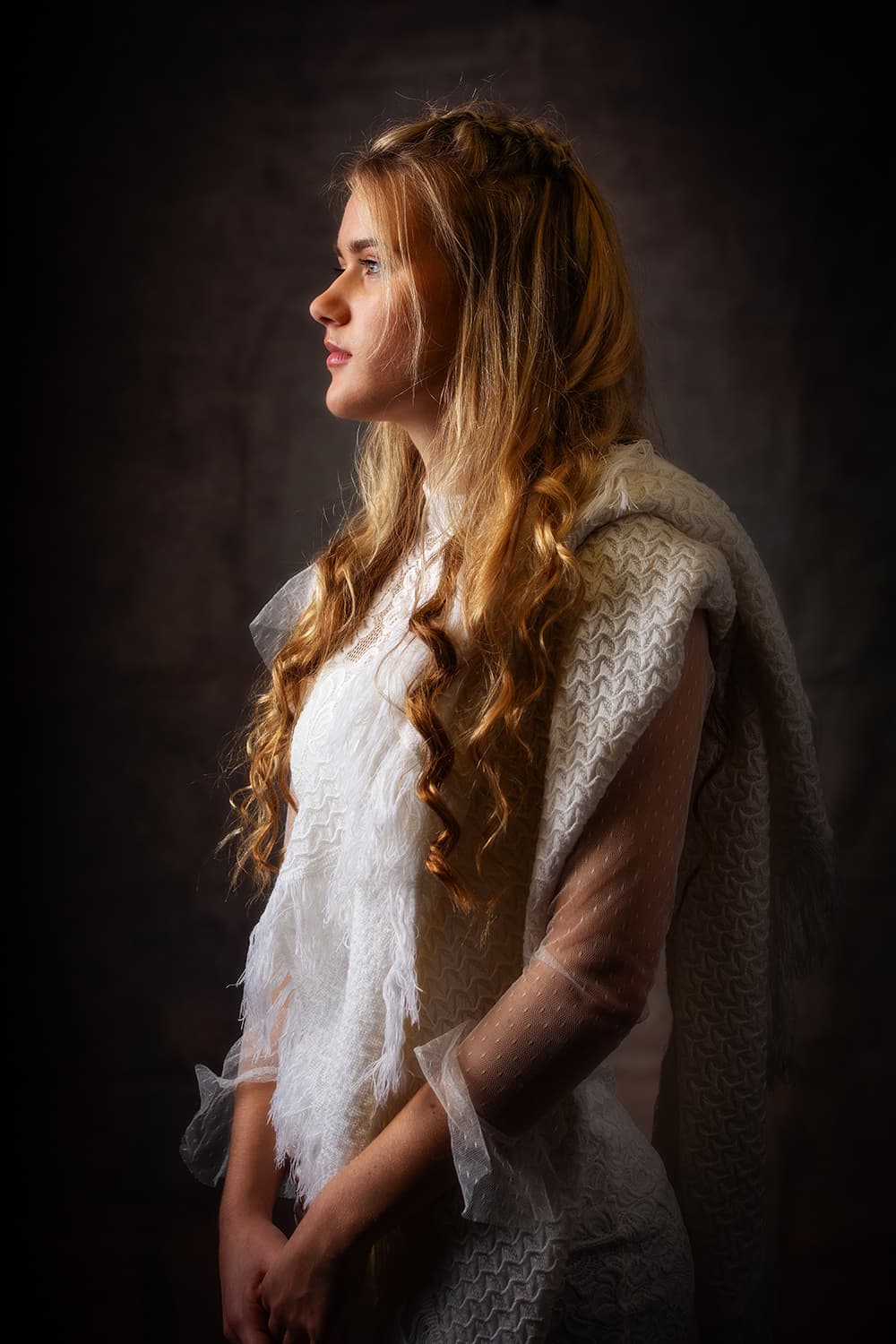 Low lit portrait of a teen profile wearing a white dress witha woollen throw over her shoulder.