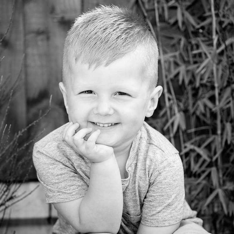 Close up black and white photo of a small boy looking at the camera resting his chin on his hand