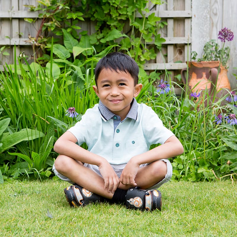 Portrait of a small asian boy sitting crossed leg in a garden.