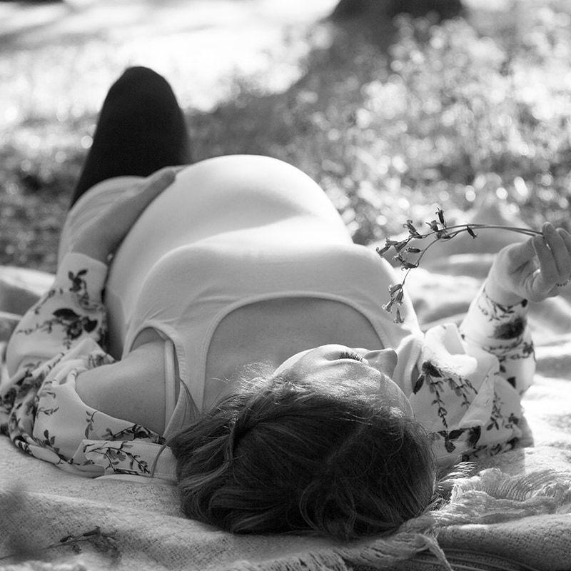 Maternity photo shoot of a pregnant woman laying on her back in a wood
