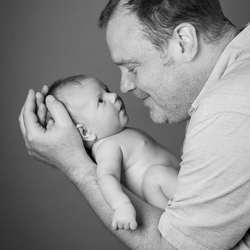 Black & white portrait of a father holding his baby newborn son in his hands close to his face
