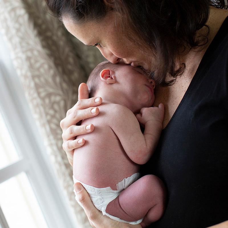 Mother holding newborn baby close by a window.