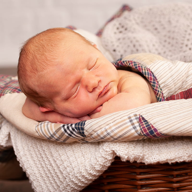 Newborn baby asleep in a basket under blankets, lying on his front