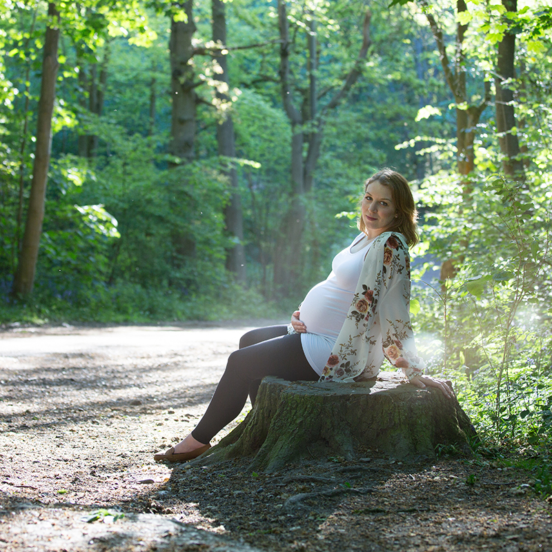 Pregant woman sitting on a log ina forest holding her tummy.