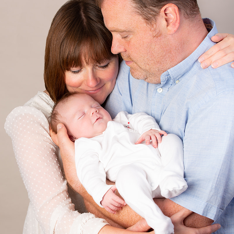 Parents cuddling newborn at a photo shoot in the studio.