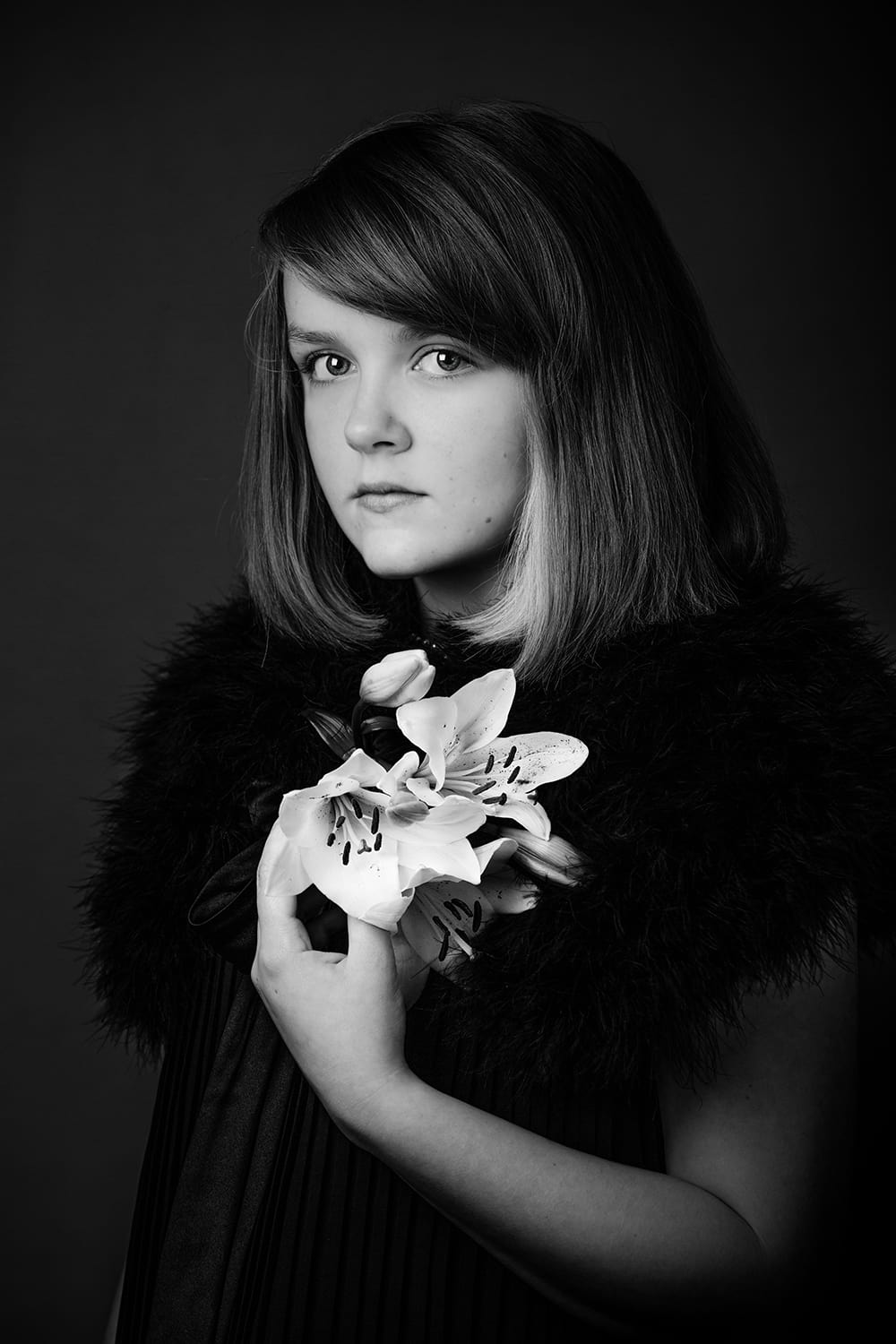 Black & white image of young teen wearing black looking at the camera holding a Lily