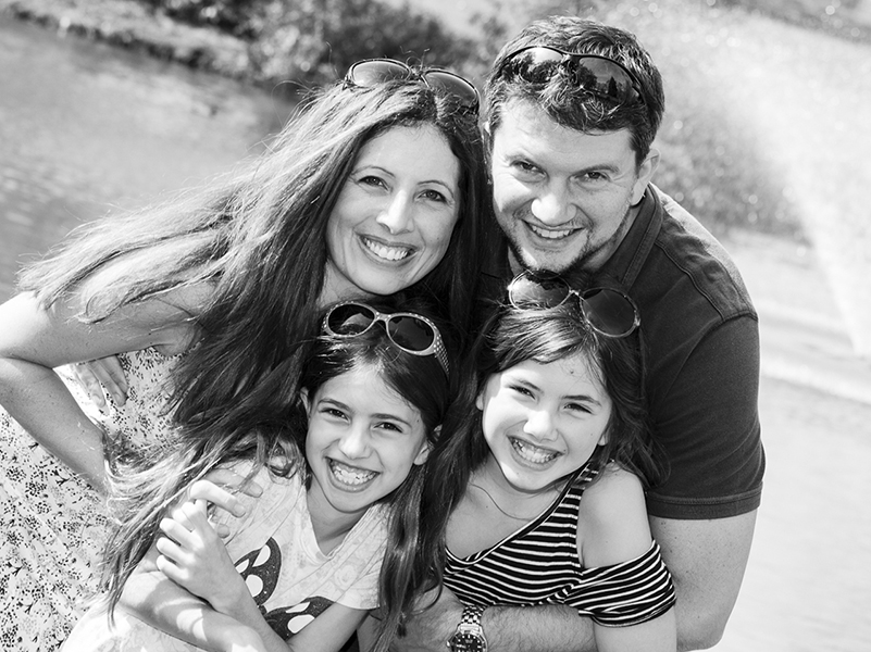 A mum and dad standing close to their two daughters cuddling together by a lake near Colchester University.