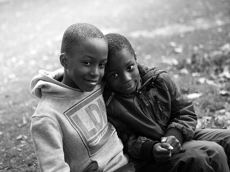 Two boys outside sitting next to and leaning in to each other.